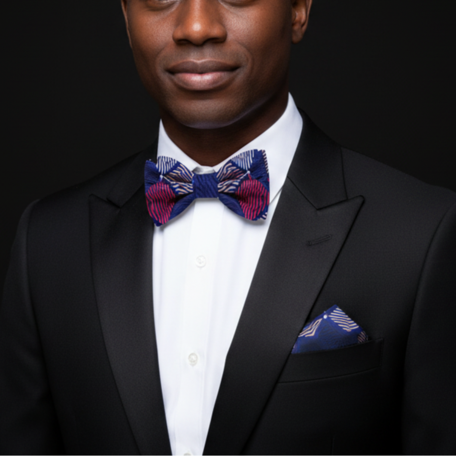 Man wearing a black suit with a colorful bow tie and pocket square on a black background