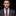 Man wearing a gray suit with a red and blue checkered tie and pocket square on a black background