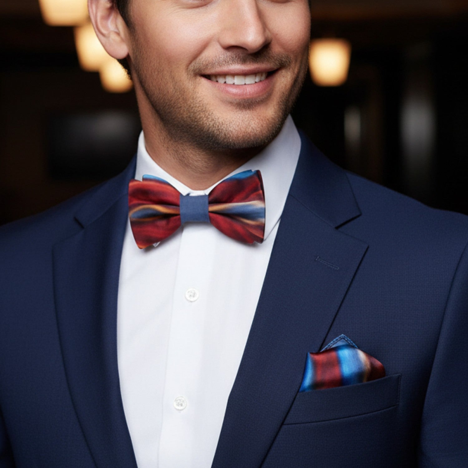 Man wearing a navy suit with a colorful bow tie and pocket square, smiling.
