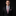 Man wearing a black suit with a red paisley tie and pocket square on a black background