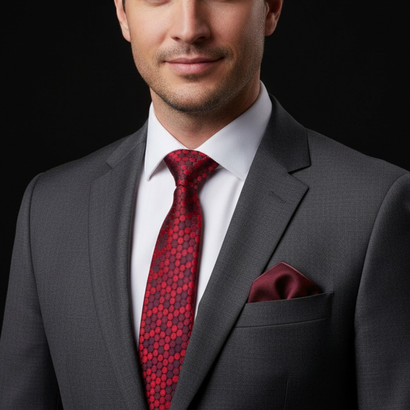 Man wearing a gray suit with a red patterned tie and matching pocket square on a black background