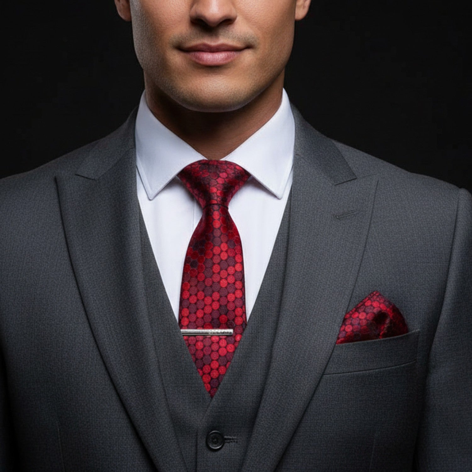 Man wearing a gray suit with a red patterned tie and pocket square on a black background