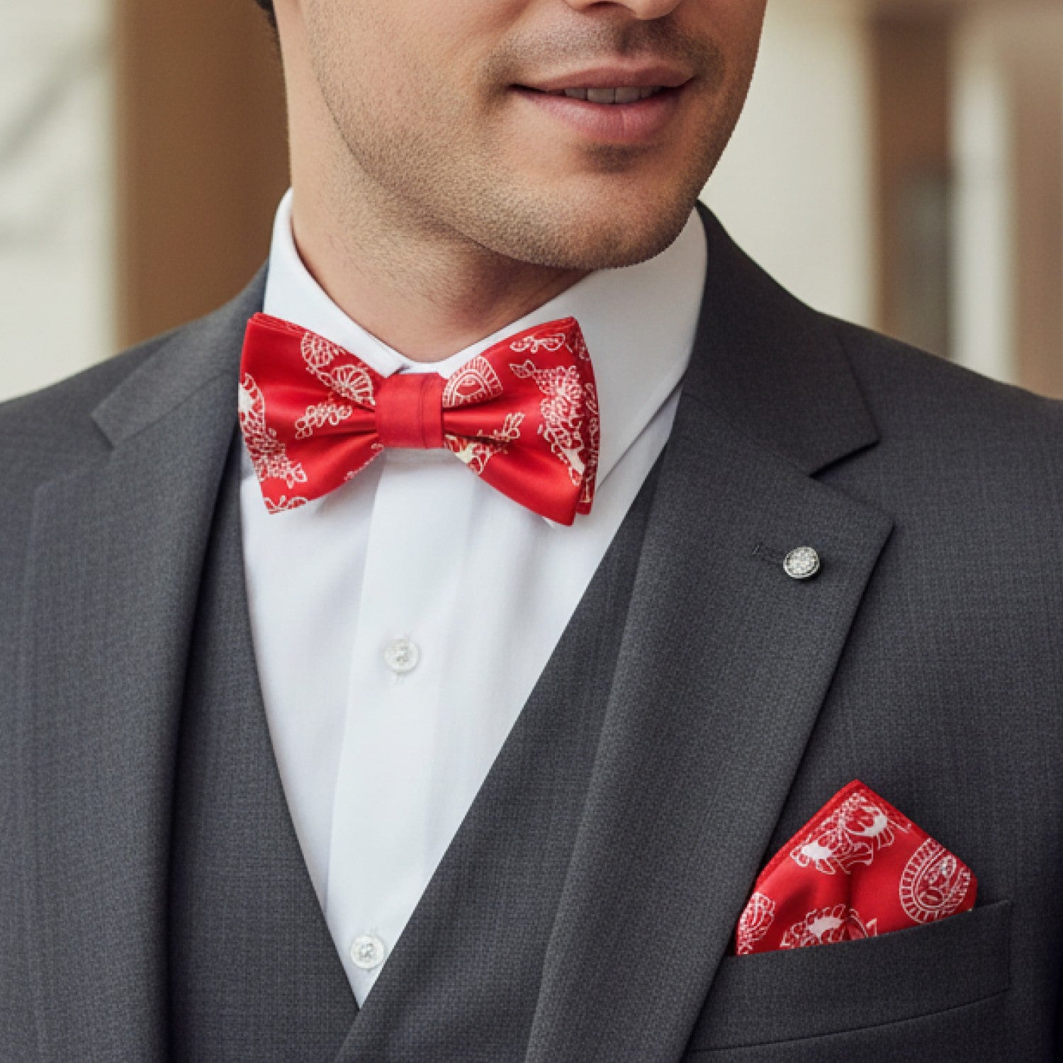 Man wearing a gray suit with a red bow tie and pocket square, blurred background