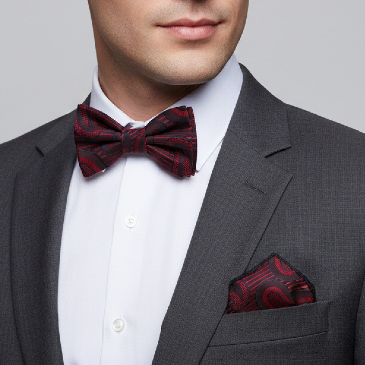 Man wearing a gray suit with a red patterned bow tie and pocket square on a light gray background