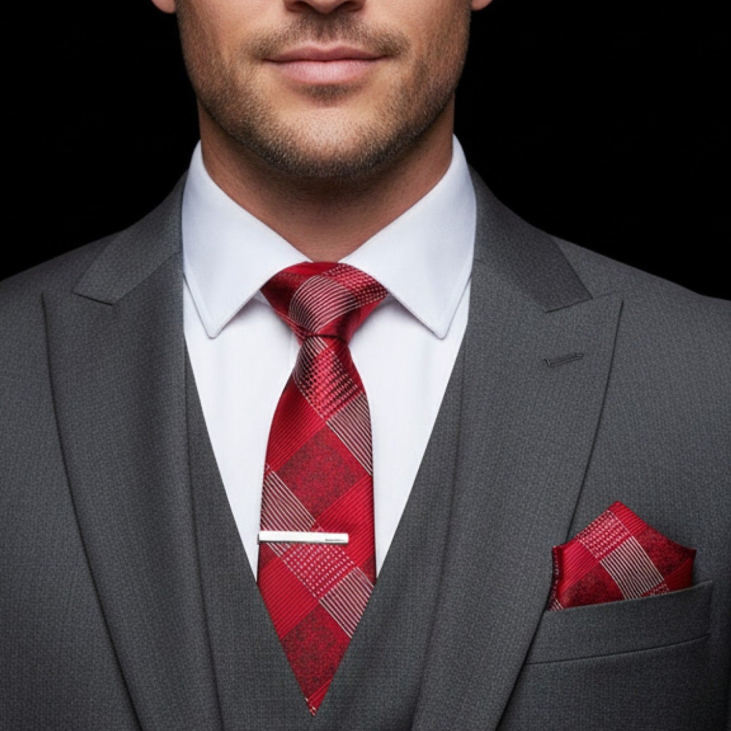 Man wearing a gray suit with a red plaid tie and pocket square on a black background