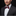 Man wearing a black suit with a white shirt and a red and gray bow tie on a dark background