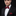 Man wearing a black suit with a red bow tie and pocket square on a dark background