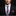 Man wearing a black suit with a blue and red checkered tie and pocket square on a dark background