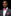 Man wearing a black suit with a pink bow tie and pocket square on a black background