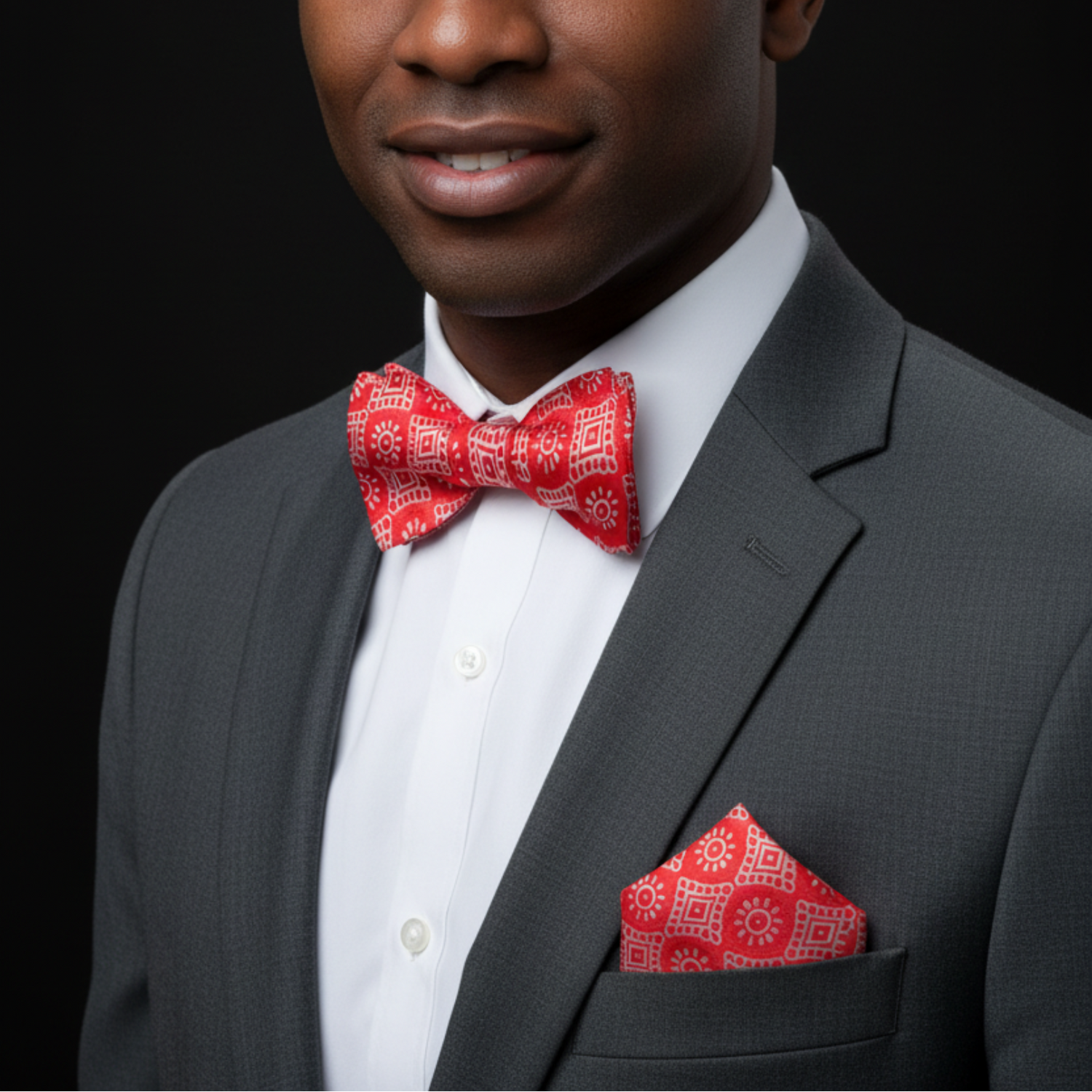 Man wearing a gray suit with a red bow tie and pocket square on a black background