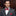 Man wearing a gray suit with a red bow tie and pocket square in an indoor setting
