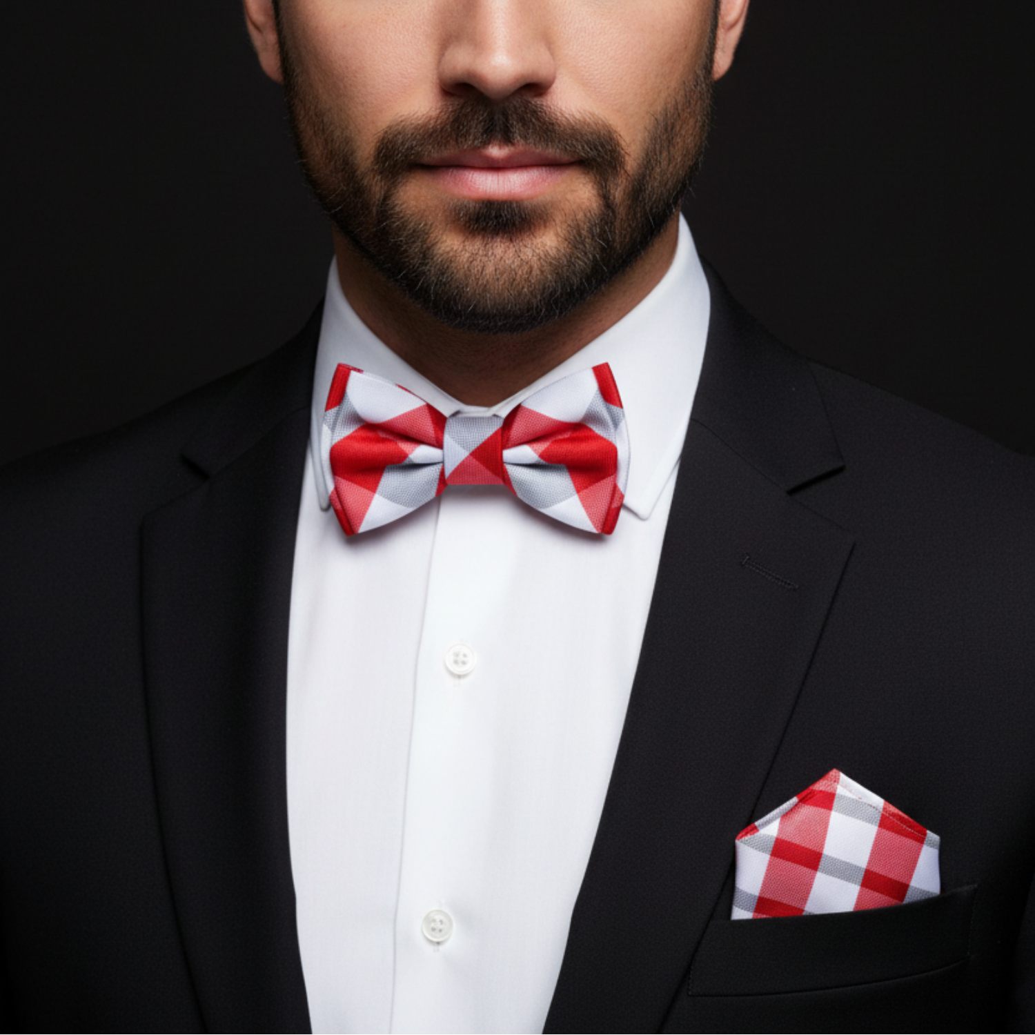 Man wearing a black suit with a red and white checkered bow tie and pocket square on a dark background