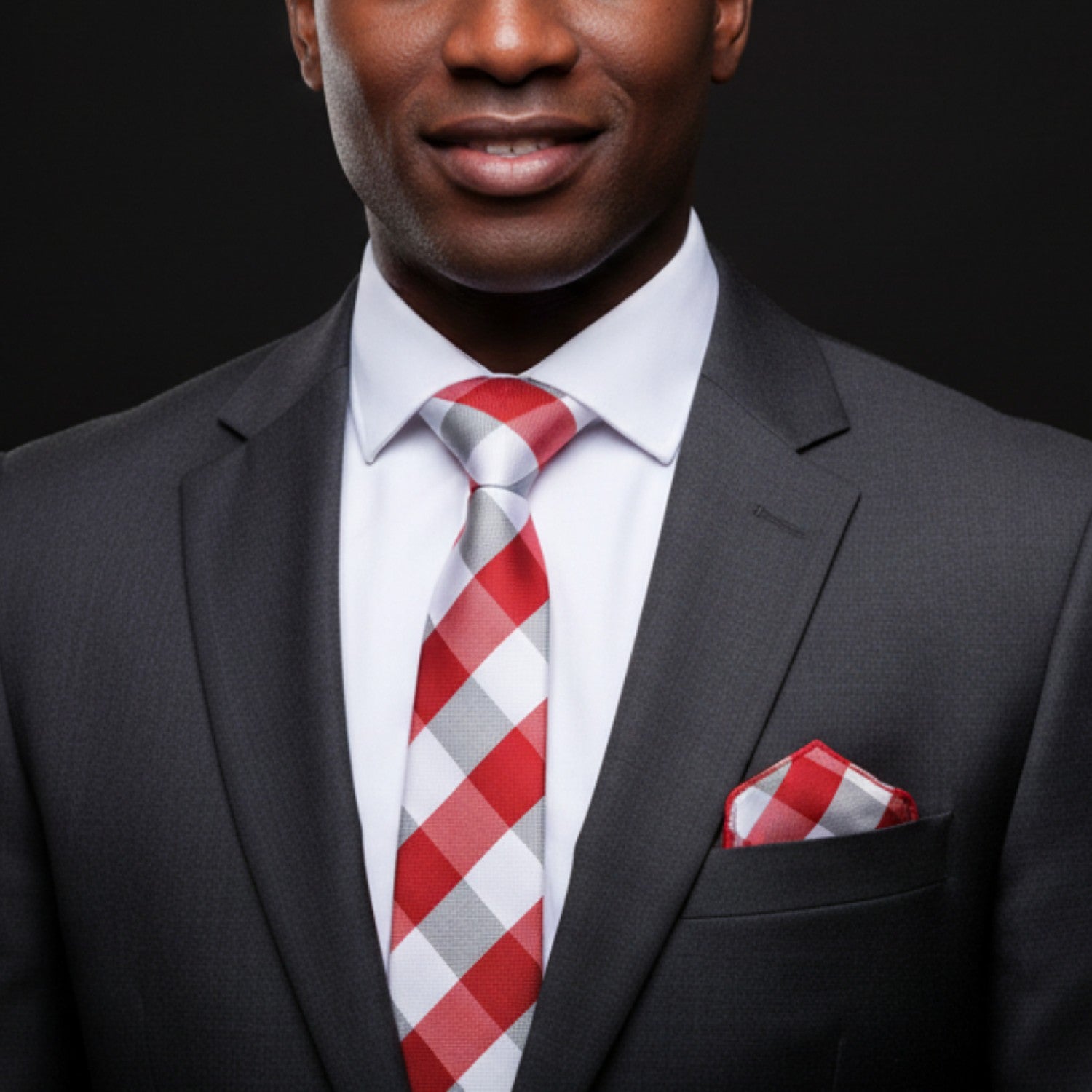 Man wearing a gray suit with a red and white checkered tie and pocket square on a black background