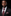Man wearing a black suit with a red tie and pocket square against a black background