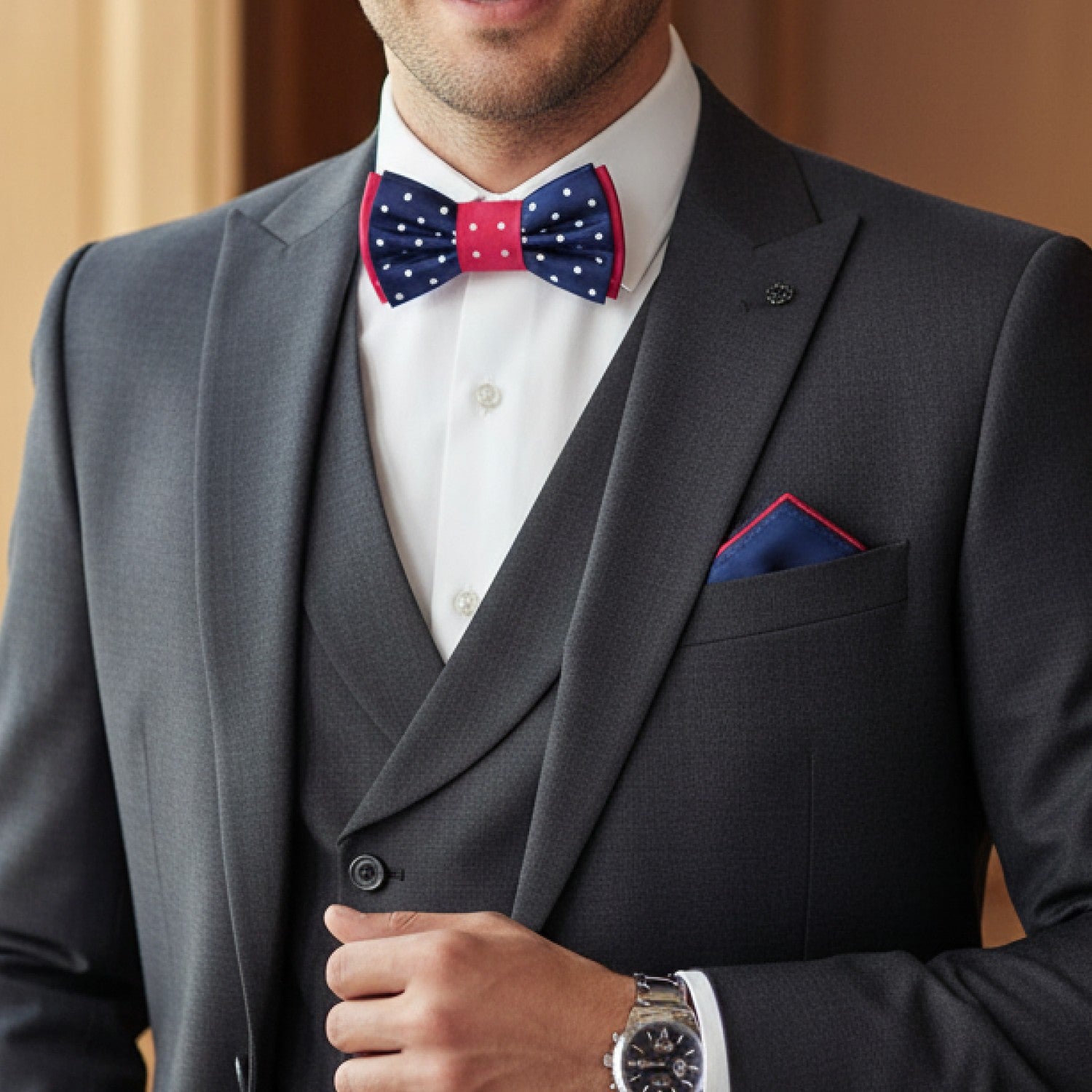 Man wearing a gray suit with a white shirt, red and blue polka dot bow tie, and matching pocket square.