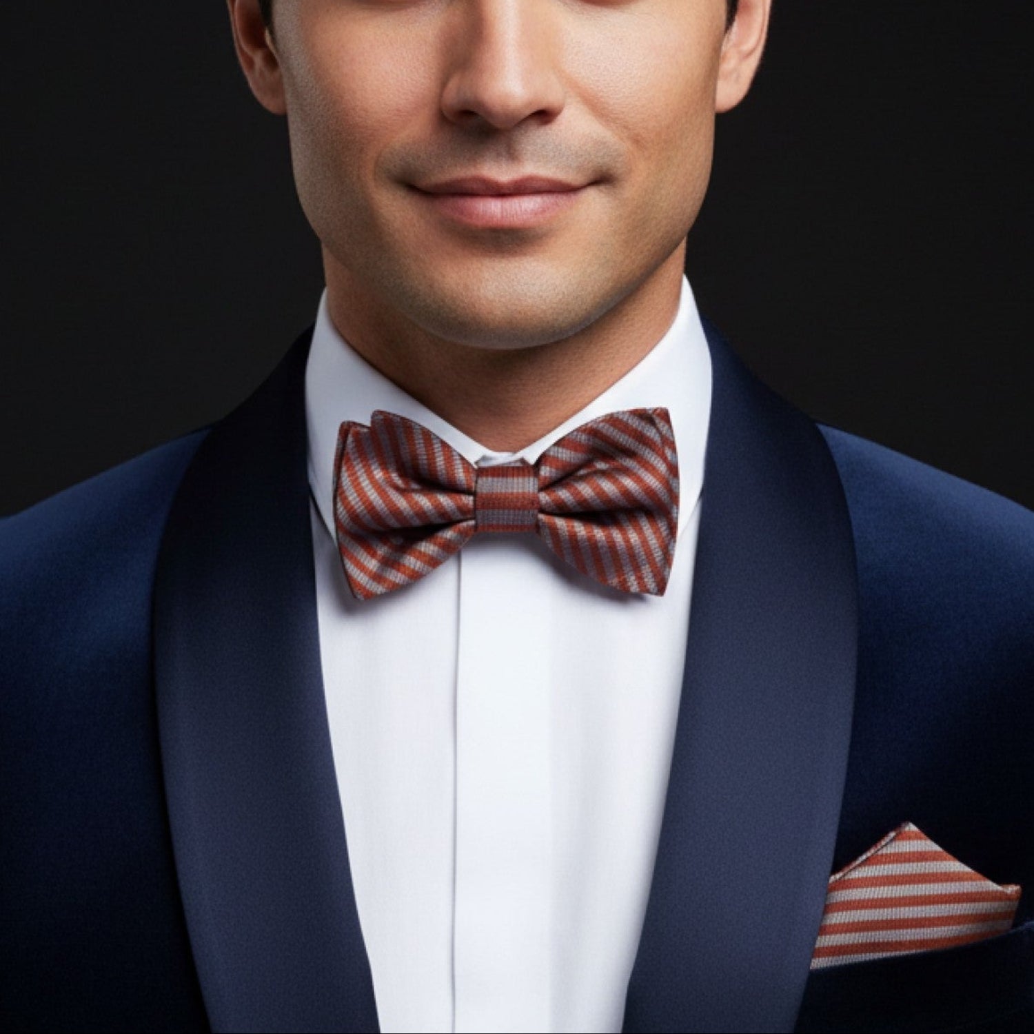 Man wearing a navy suit with a red and white striped bow tie and pocket square on a black background