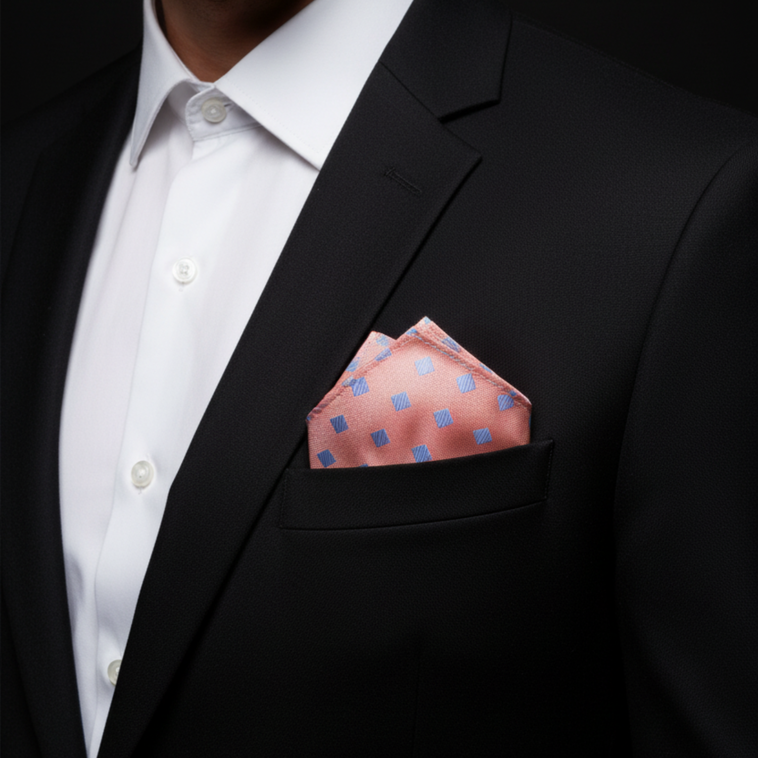Man wearing a black suit with a white shirt and pink pocket square against a dark background
