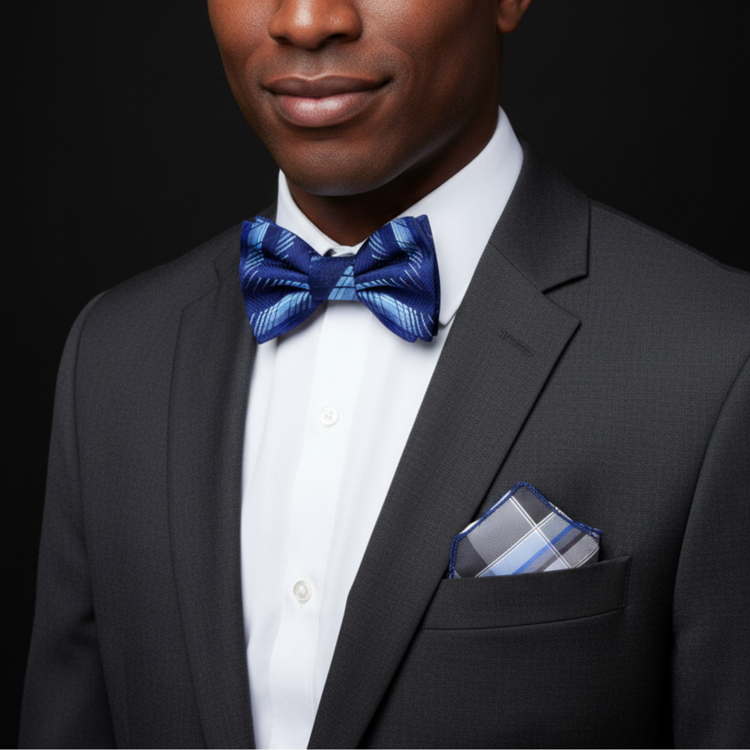 Man wearing a black suit with a blue bow tie and pocket square on a dark background