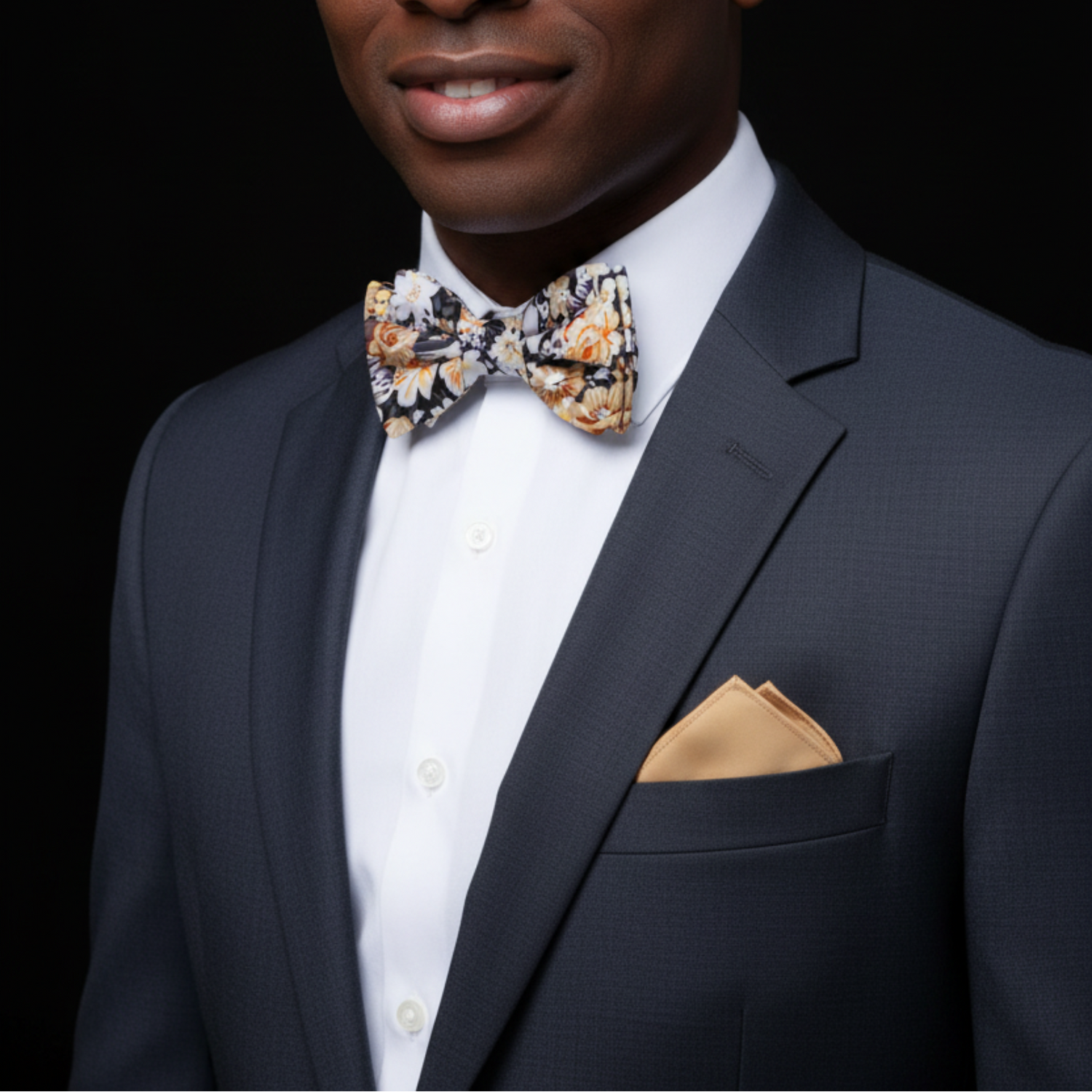 Man wearing a navy suit with a floral bow tie and beige pocket square on a black background