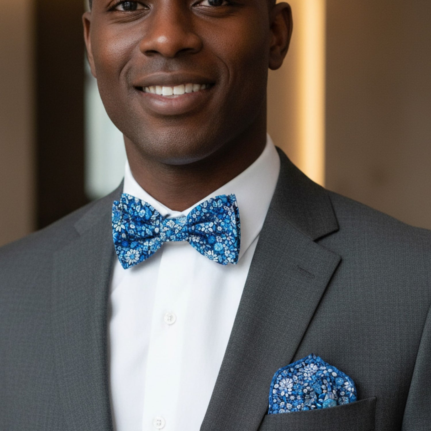 Man wearing a gray suit with a blue bow tie and pocket square, smiling.