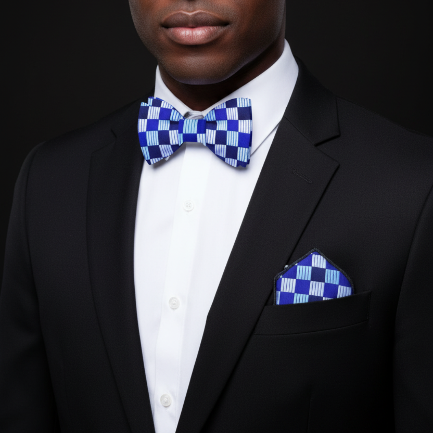 Man wearing a black suit with a blue and white checkered bow tie and pocket square.