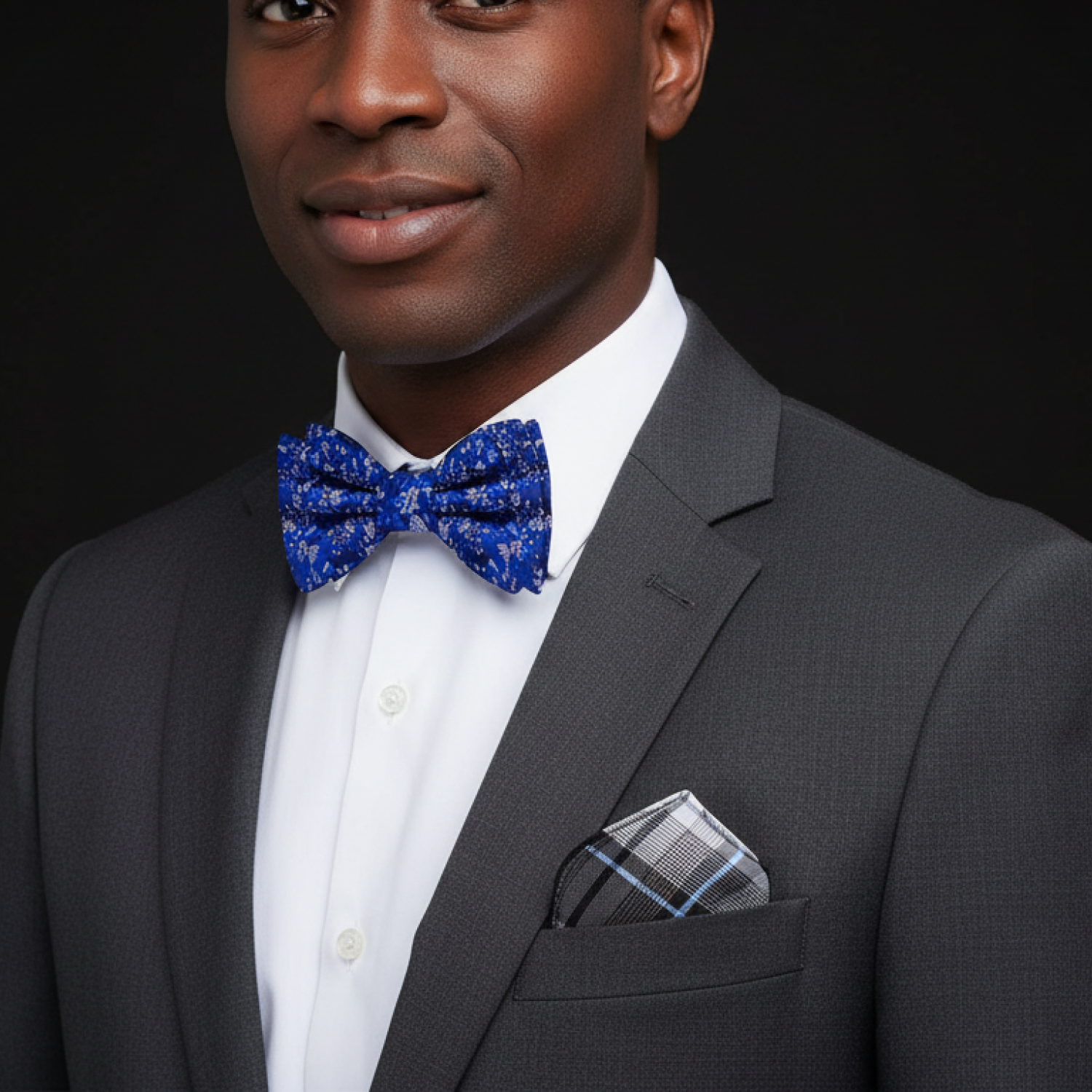 Man wearing a gray suit with a blue bow tie and pocket square on a black background