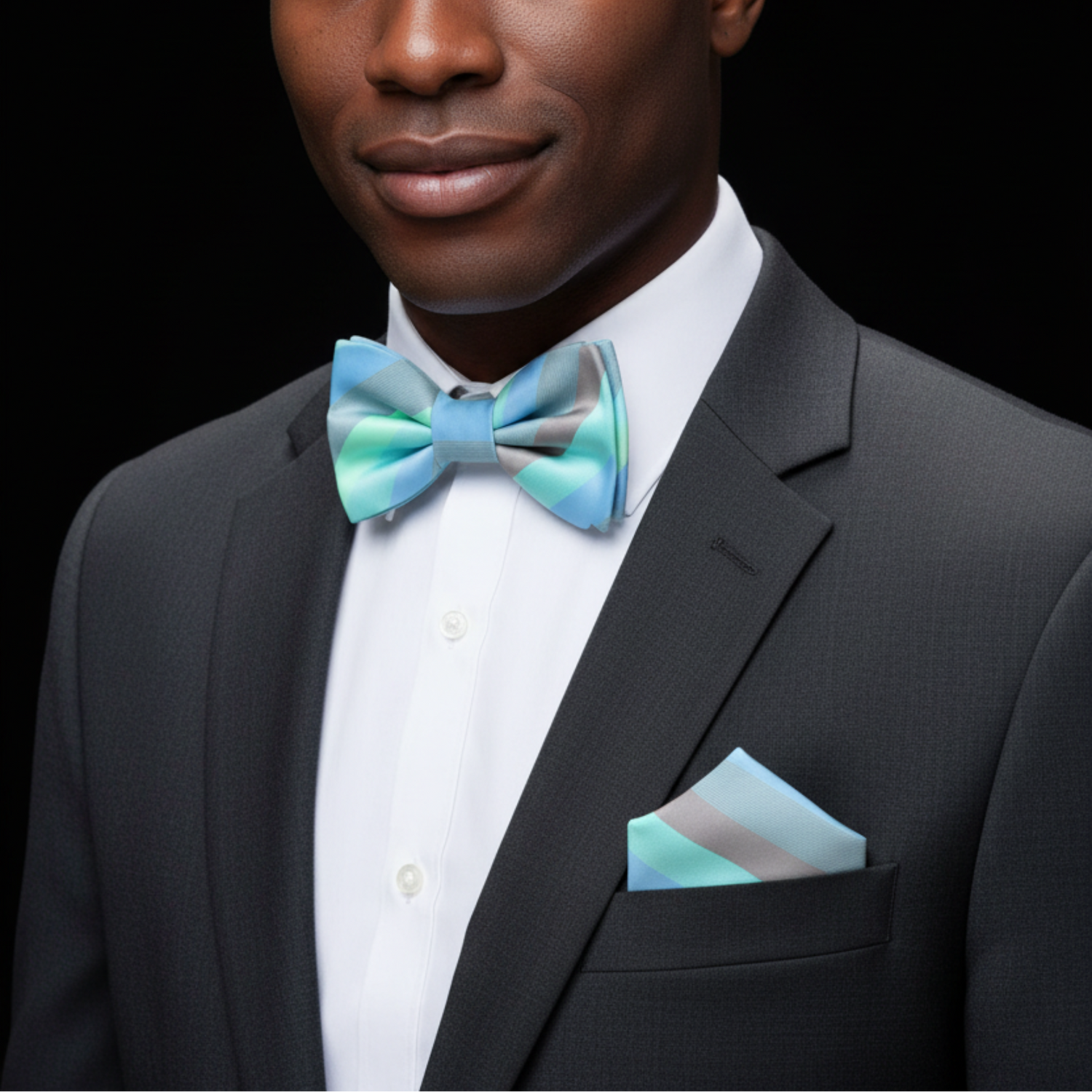 Man wearing a black suit with a light blue bow tie and pocket square on a black background