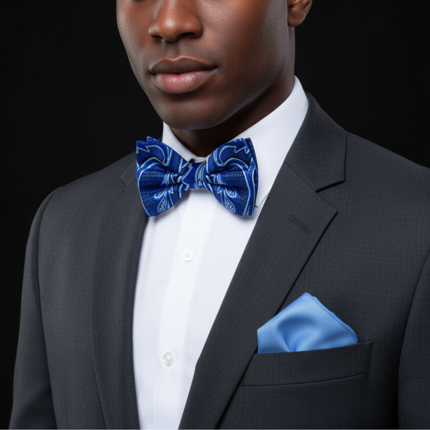 Man wearing a gray suit with a blue bow tie and pocket square on a black background