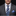 Man wearing a gray suit with a blue striped tie and pocket square on a black background