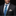 Man wearing a black suit with a blue paisley tie and patterned pocket square on a dark background