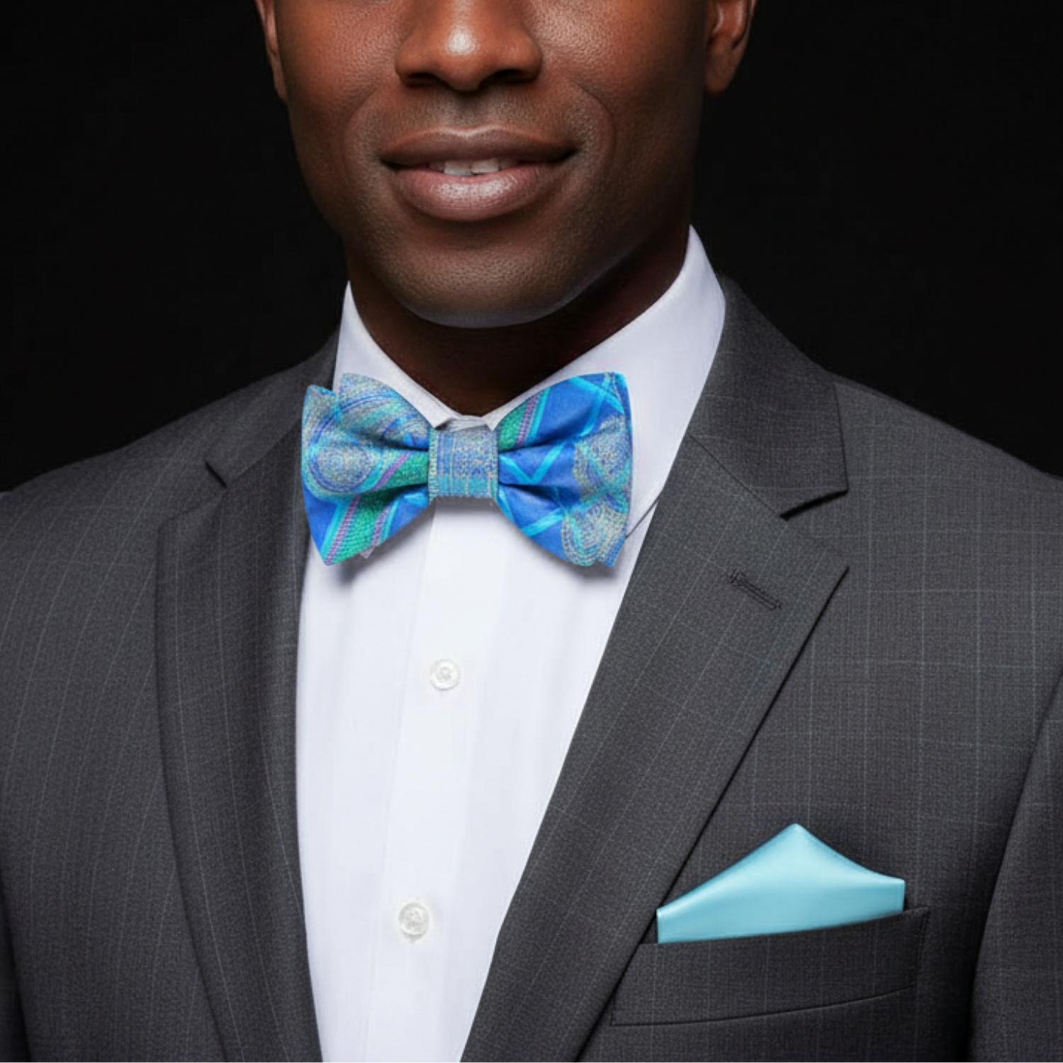 Man wearing a gray suit with a blue bow tie and pocket square on a black background