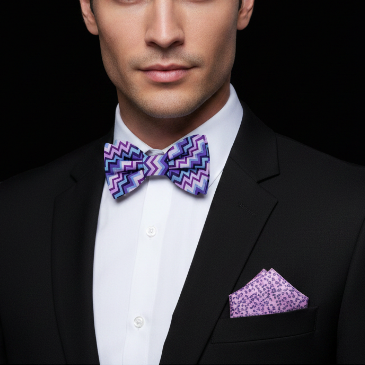 Man wearing a black suit with a purple and blue zigzag bow tie and matching pocket square.