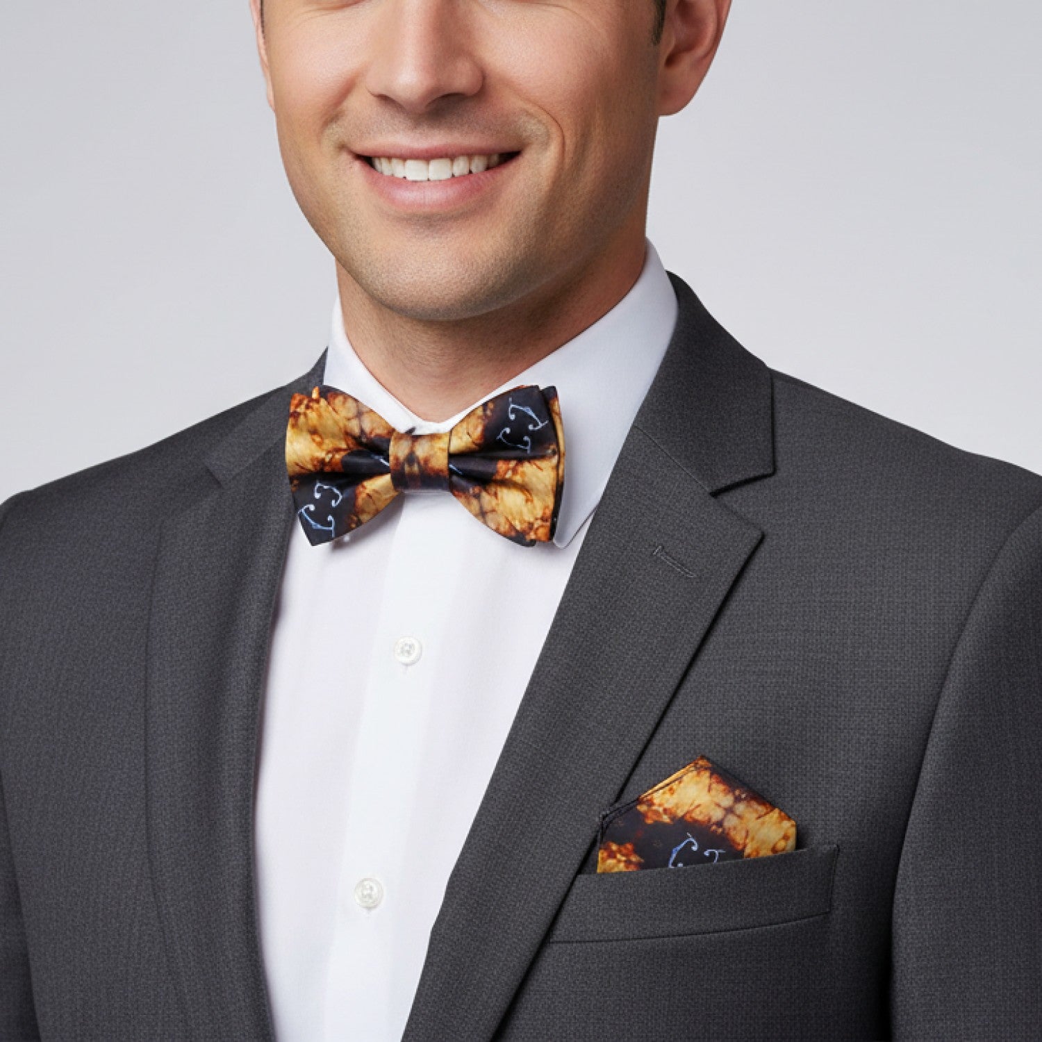 Man wearing a gray suit with a patterned bow tie and pocket square on a plain background