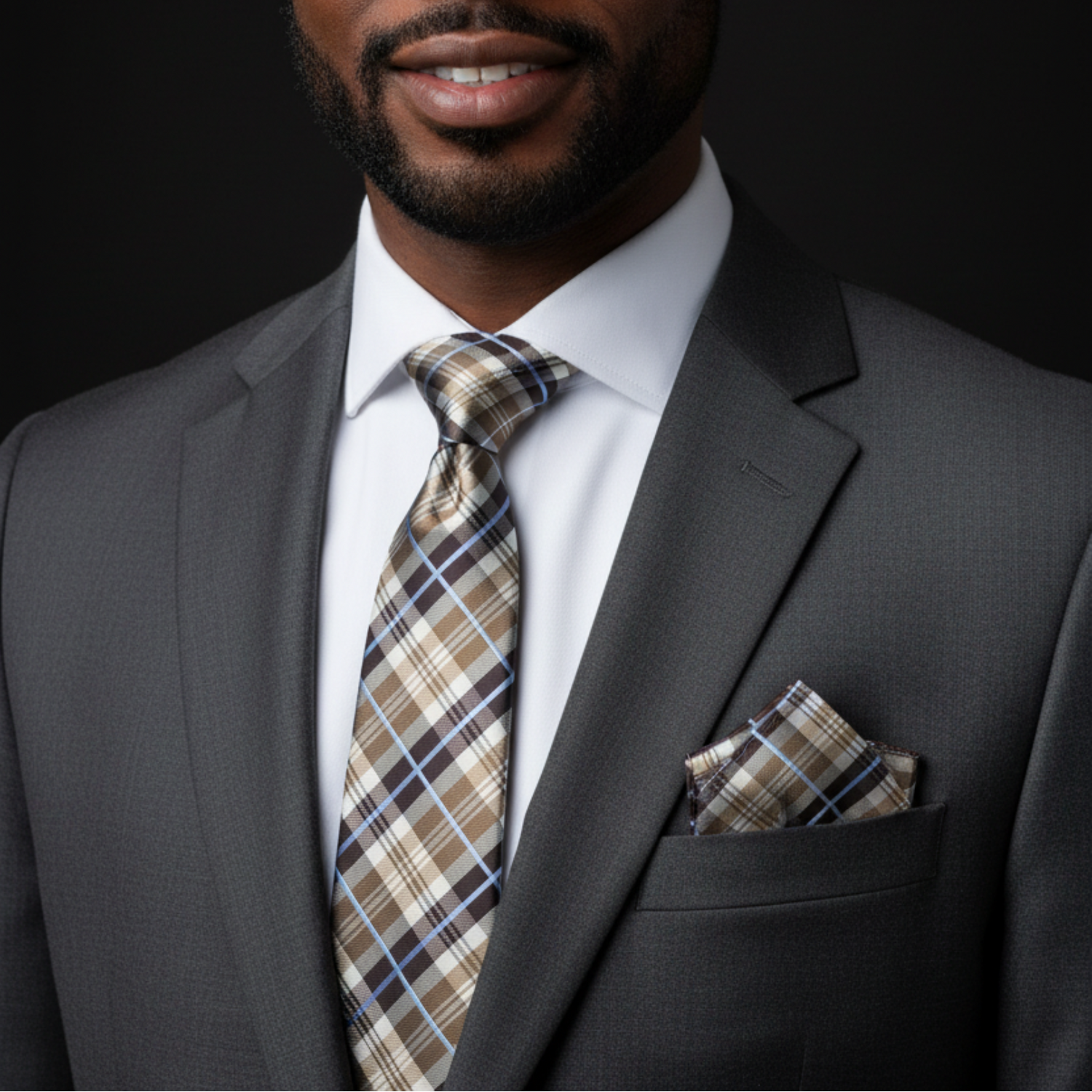Man wearing a gray suit with a plaid tie and pocket square against a black background