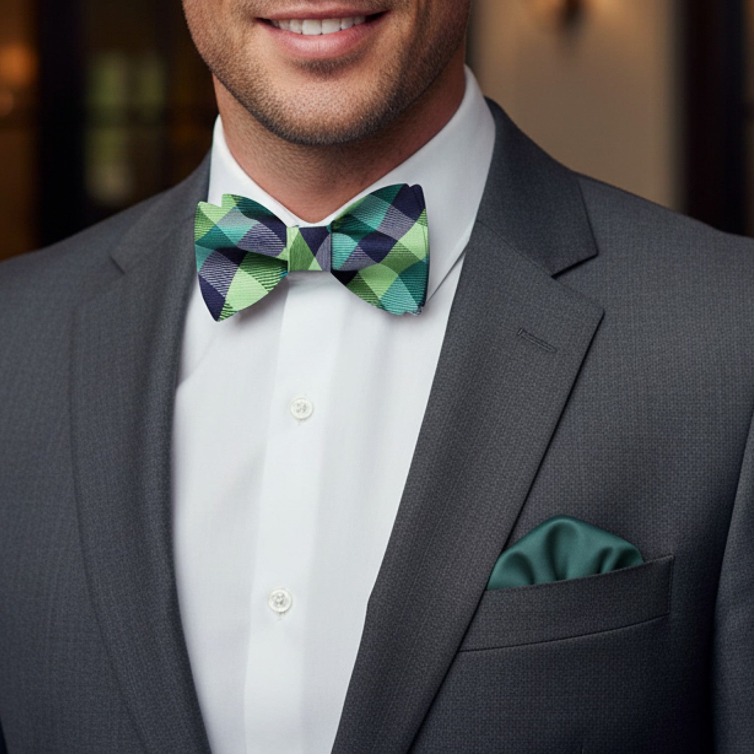 Man wearing a gray suit with a green checkered bow tie and matching pocket square.
