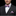 Man wearing a black suit with a pink and blue checkered bow tie and pocket square on a black background