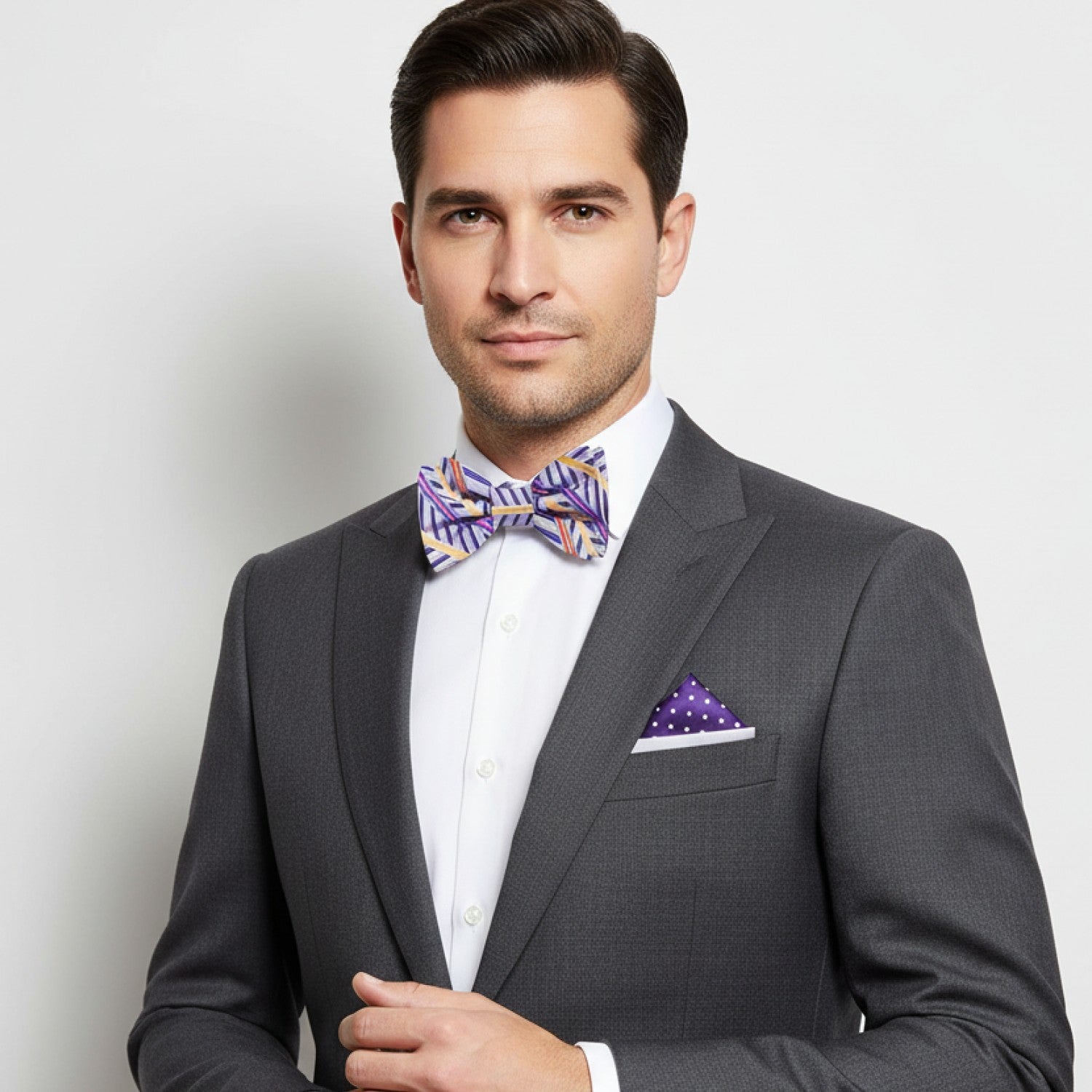 Man wearing a gray suit with a colorful bow tie and pocket square on a light background