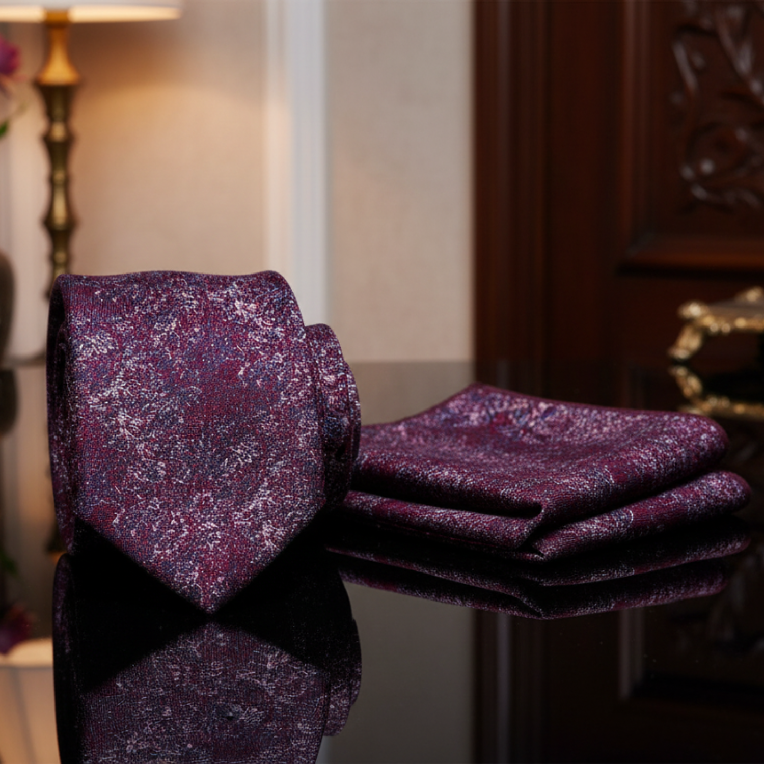 red and blue patterned tie and pocket square set on a reflective surface with a blurred background