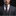 Man wearing a gray suit with a purple tie and pocket square against a black background