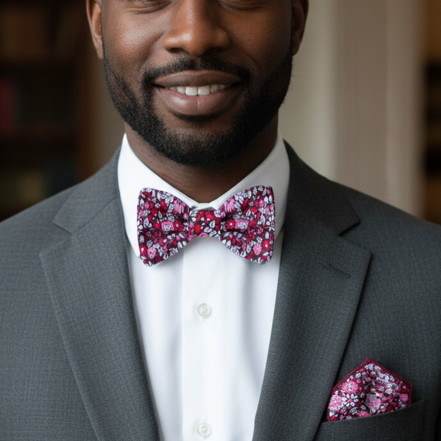 Man wearing a gray suit with a red, pink floral bow tie and pocket square.