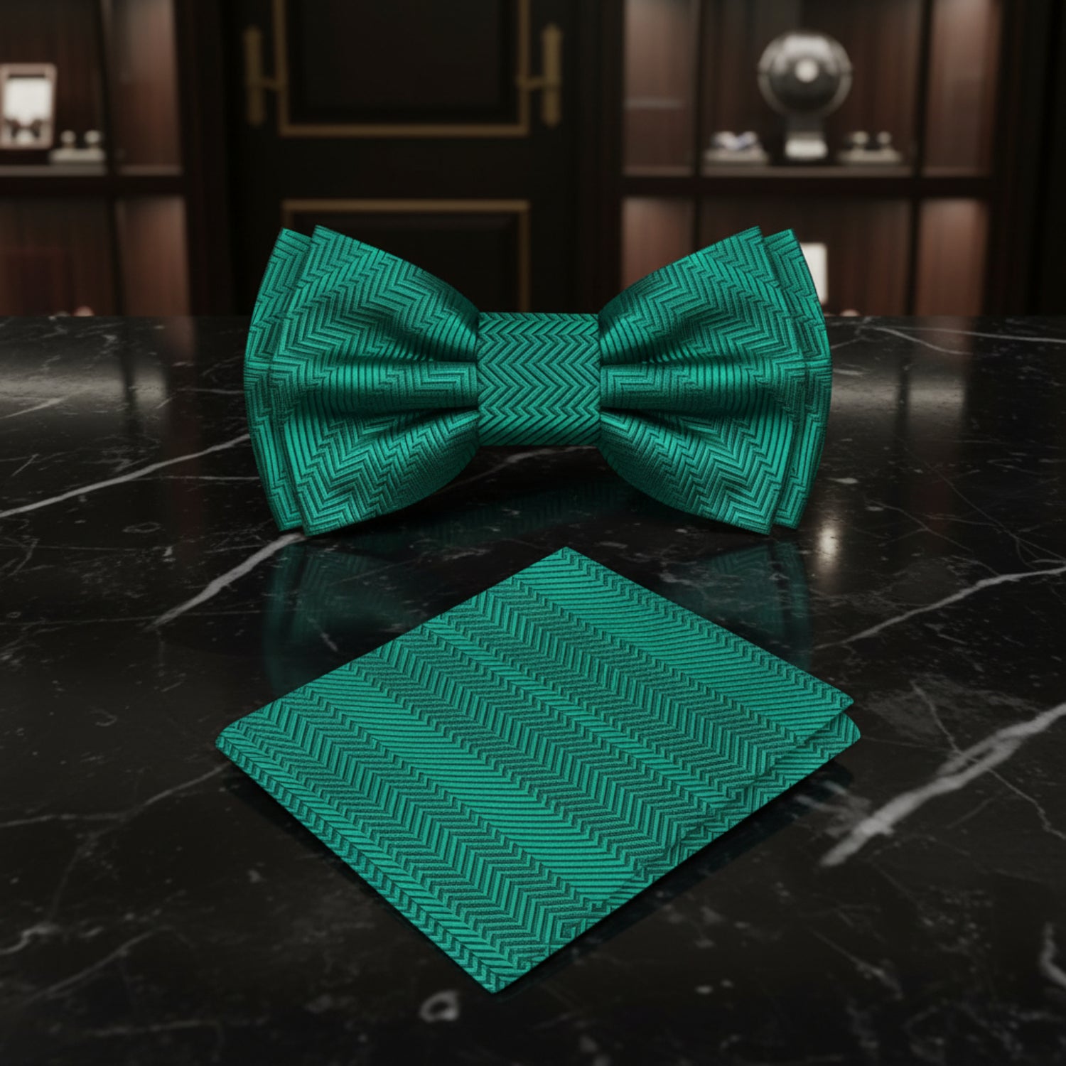 Teal bow tie and matching pocket square on a dark marble surface with wooden frames in the background.