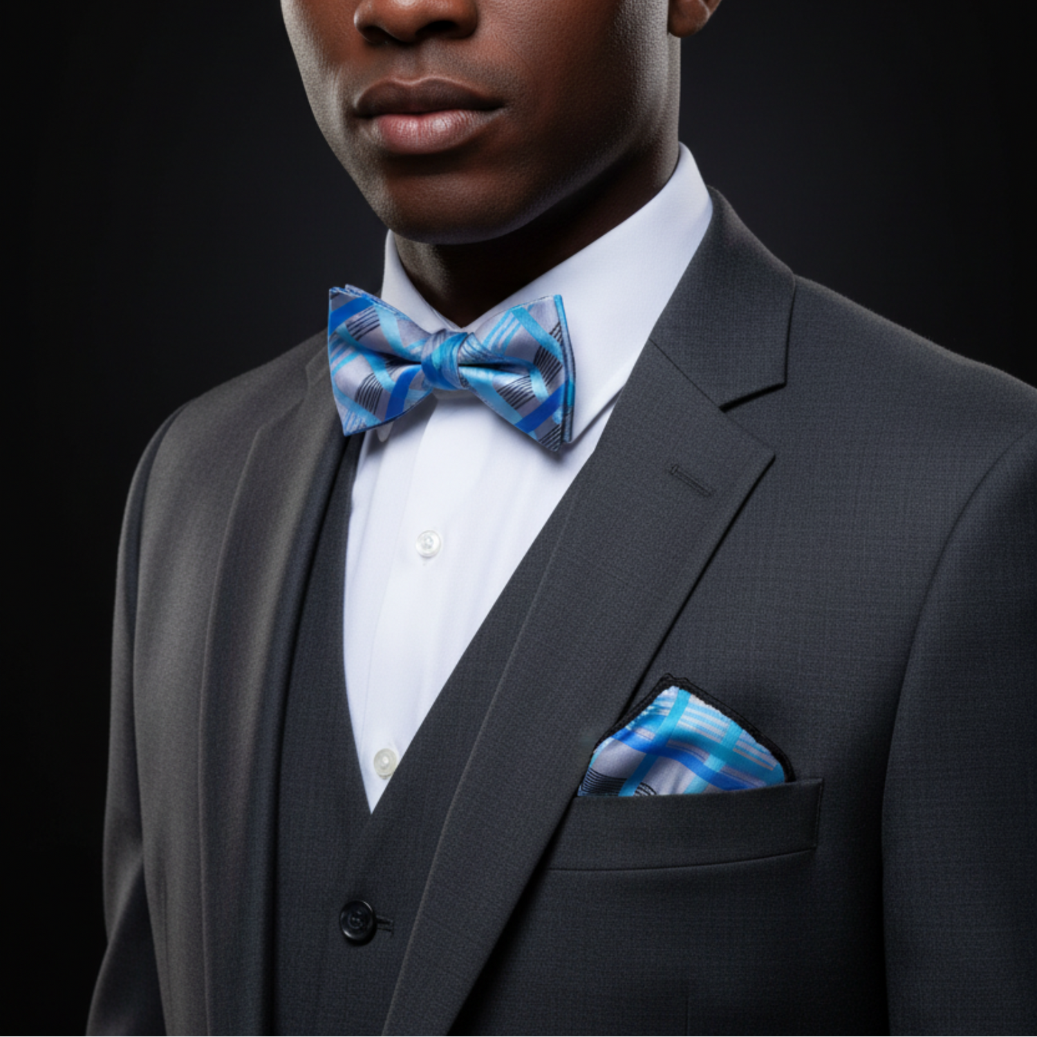 Man wearing a gray suit with a blue checkered bow tie and pocket square on a black background