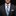 Man wearing a dark suit with a blue plaid tie and pocket square on a black background