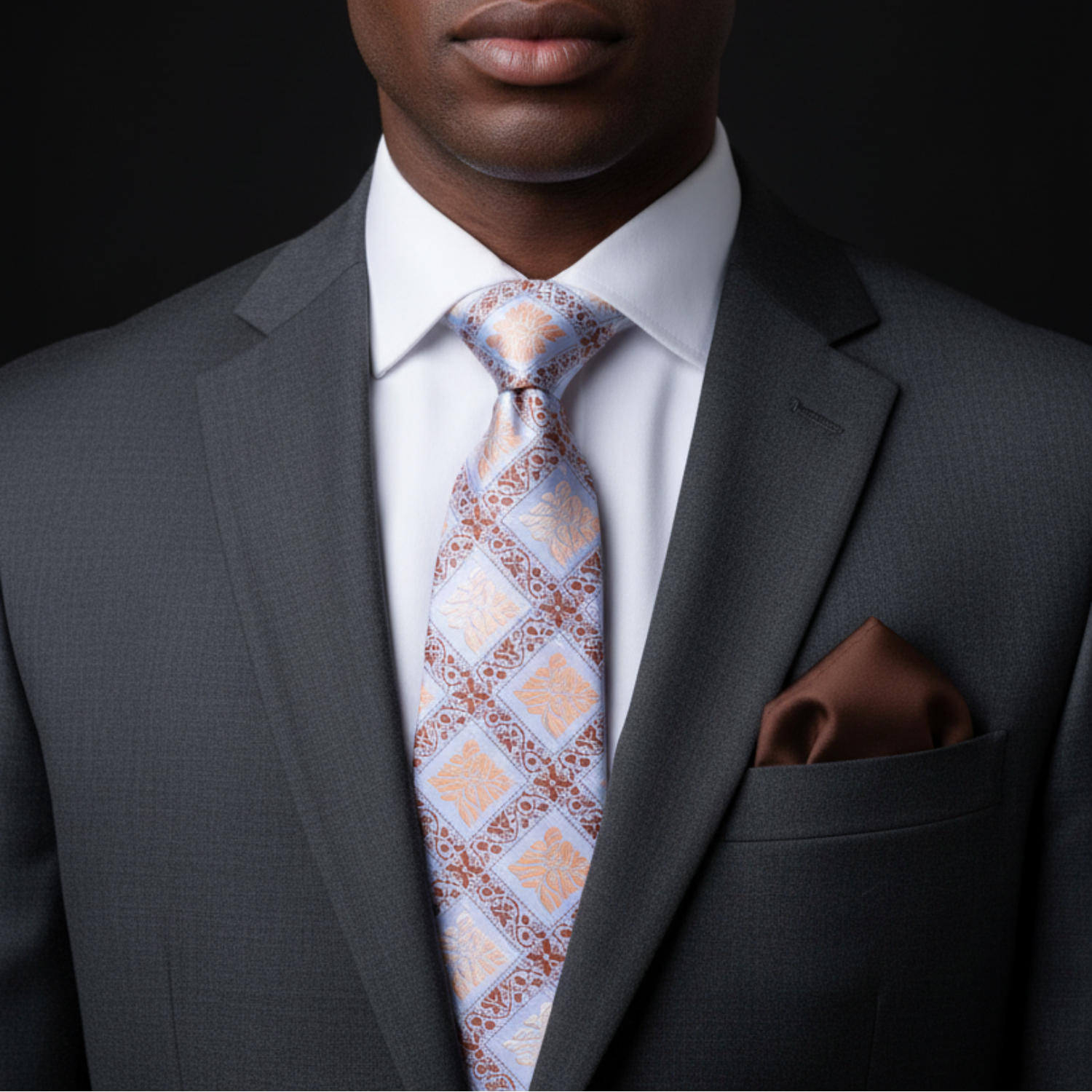 Man wearing a gray suit with a patterned tie and brown pocket square on a black background