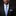 Man wearing a black suit with a blue tie and light blue pocket square on a dark background