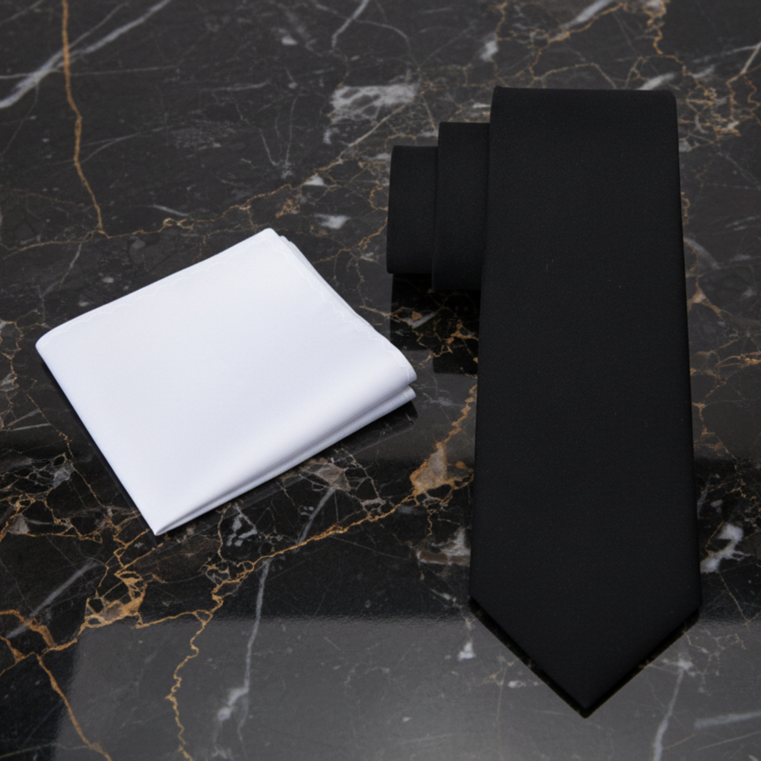 Black tie and white pocket square on a black marble surface