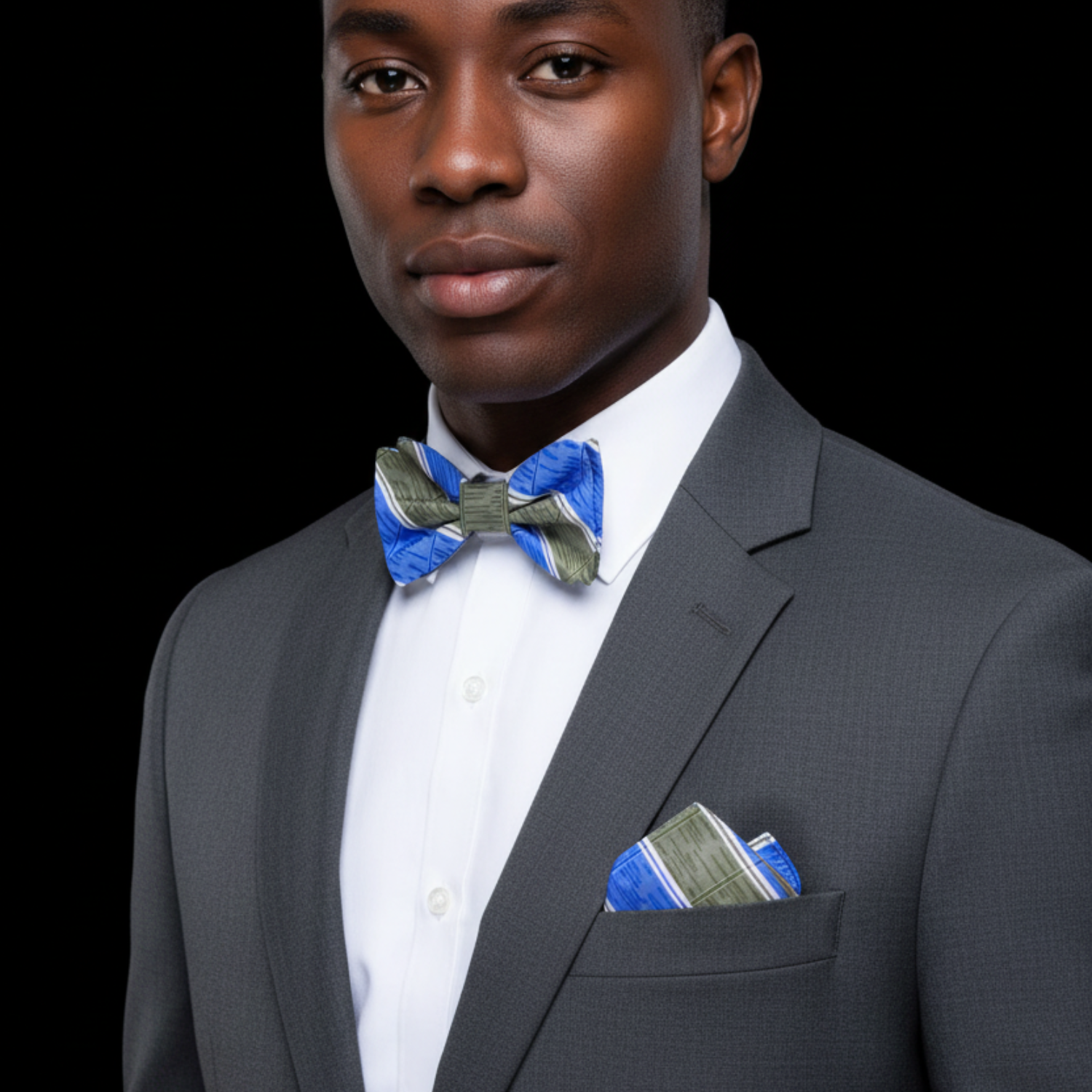Man wearing a gray suit with a blue and green bow tie and pocket square on a black background