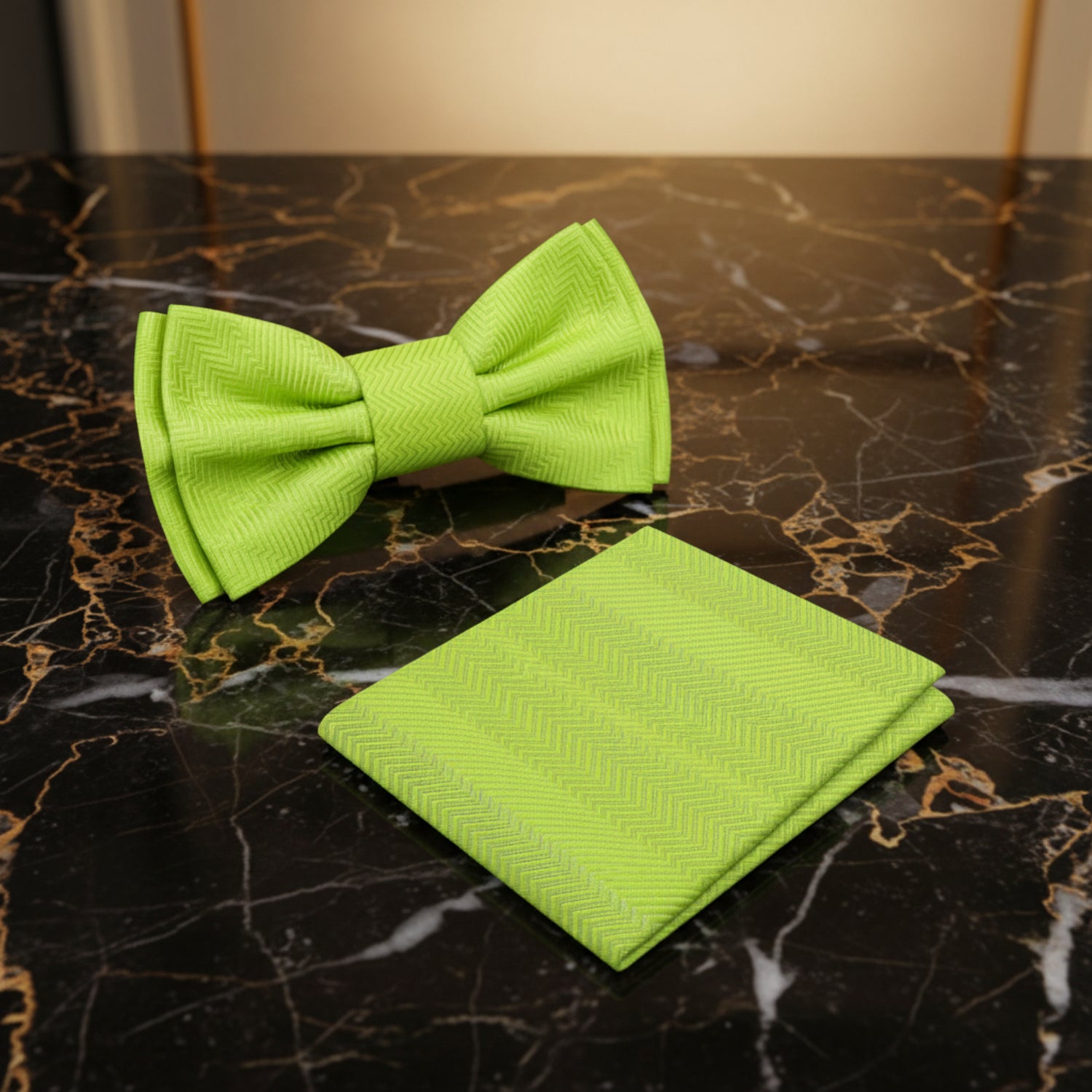 Green bow tie and matching pocket square on a dark marble surface with a blurred room background.