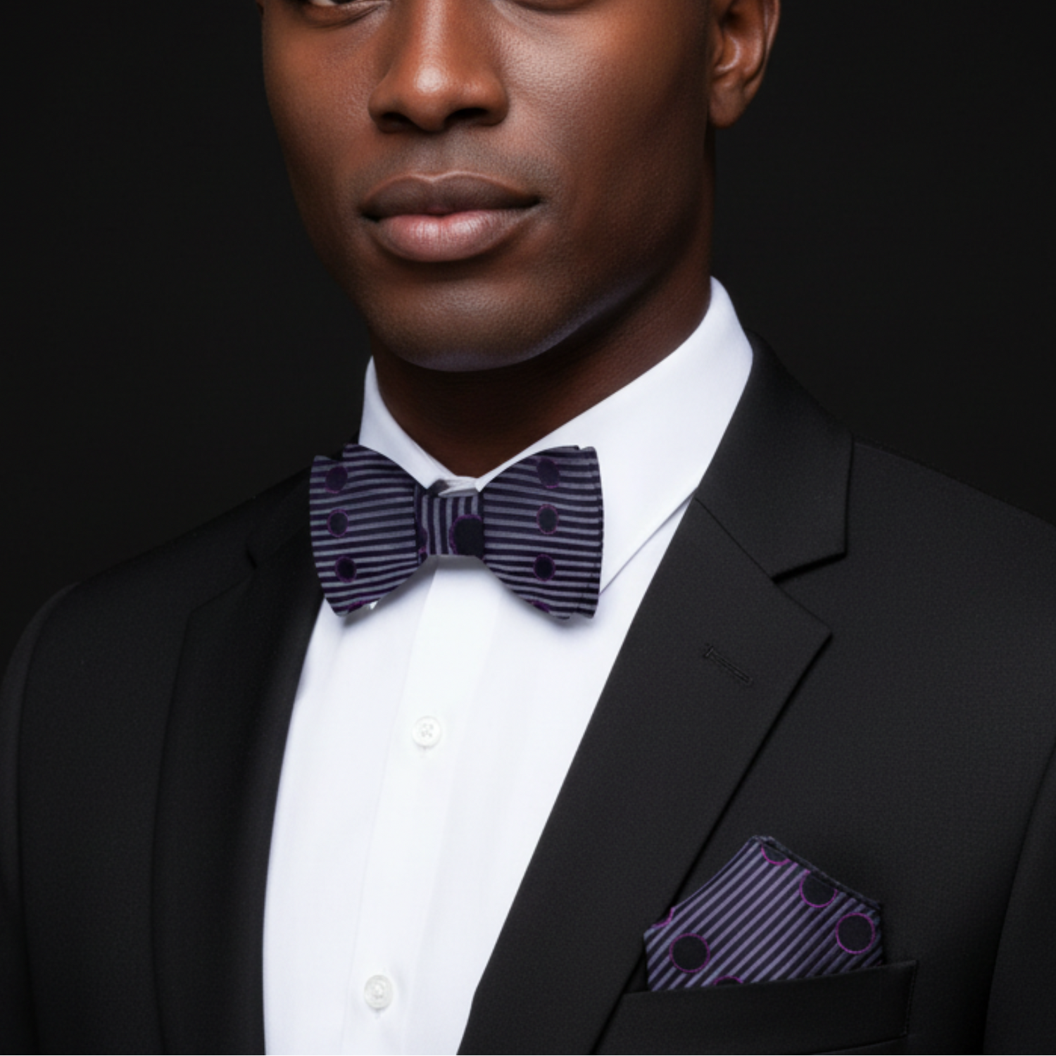 Man wearing a black suit with a purple bow tie and pocket square against a dark background