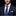 Man wearing a navy suit with a blue patterned tie and pocket square on a black background